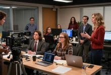 Cena documental em um escritório moderno inspirado em The Office, com mesas de trabalho, câmera de filmagem e personagens reunidos em clima de comédia
