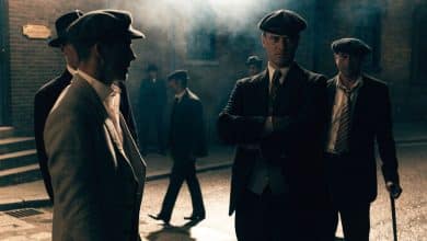 Retrato cinematográfico de um grupo fictício de gângsteres britânicos dos anos 1920 em uma rua industrial de tijolos, com ternos elegantes, boinas, fumaça e iluminação dramática.