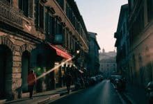 Composição cinematográfica de uma rua italiana ao entardecer, com fachadas históricas de Roma e Nápoles, uma televisão ao fundo e clima de drama contemporâneo