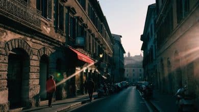Composição cinematográfica de uma rua italiana ao entardecer, com fachadas históricas de Roma e Nápoles, uma televisão ao fundo e clima de drama contemporâneo