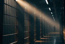 Interior de uma prisão de segurança máxima com corredores de celas, grades, luz dramática e uma figura solitária ao fundo, evocando séries de drama prisional.